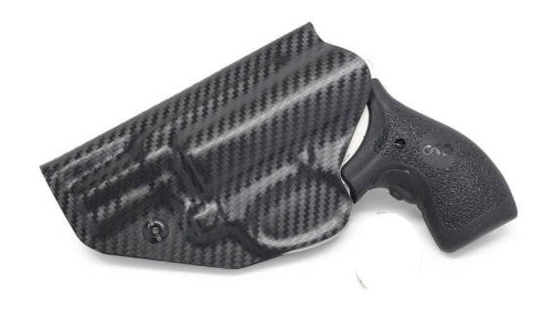 May include: A black carbon fiber holster with a textured pattern. The holster is designed to hold a black handgun grip. The grip has a textured surface and the letters "S&W" are visible.