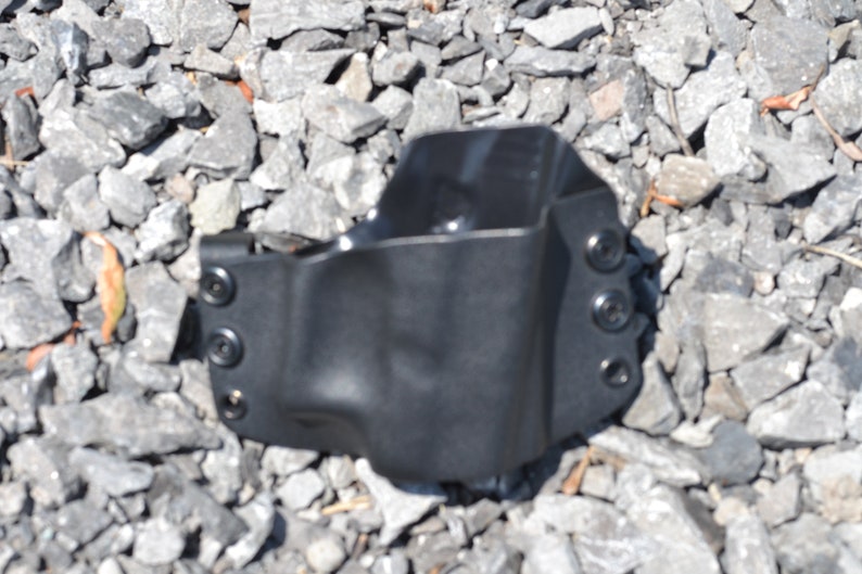 Puede incluir: Una funda de cuero negra con cuatro broches met&aacute;licos. La funda est&aacute; sobre una cama de grava gris.