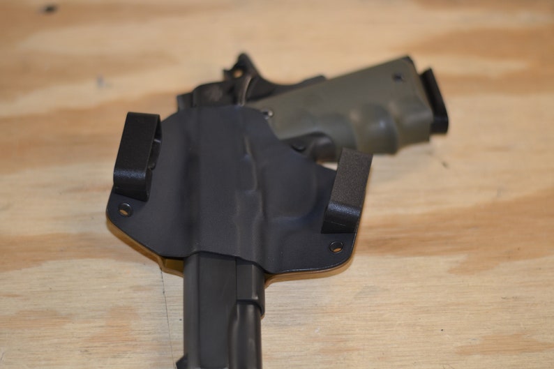Puede incluir: Una funda de cuero negra con una pistola negra en su interior. La funda tiene dos clips en la parte posterior y un peque&ntilde;o lazo en el lateral.