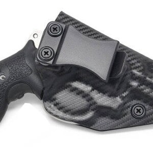 May include: Black handgun in a black and gray patterned holster. The holster has a belt clip and is secured with screws. The handgun grip has a textured surface for a secure hold.