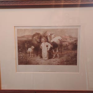 May include: Sepia-toned framed print depicting a child surrounded by a lion, lamb, and cows. The artwork has a classical style, with detailed rendering of the animals and figures. The frame is dark brown with ornate detailing.