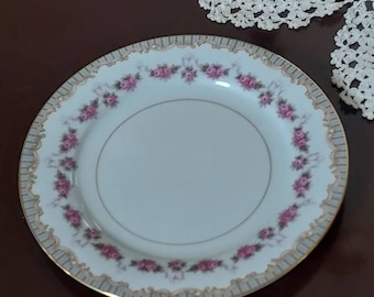May include: A white porcelain plate with a gold rim and a delicate floral pattern in pink and green. The plate has a scalloped edge and is perfect for serving desserts or appetizers.