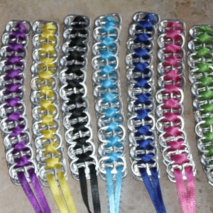 May include: A collection of handmade bracelets crafted from recycled aluminum can tabs. Each bracelet features a unique color of satin ribbon woven through the tabs, including purple, yellow, black, blue, pink, and green.