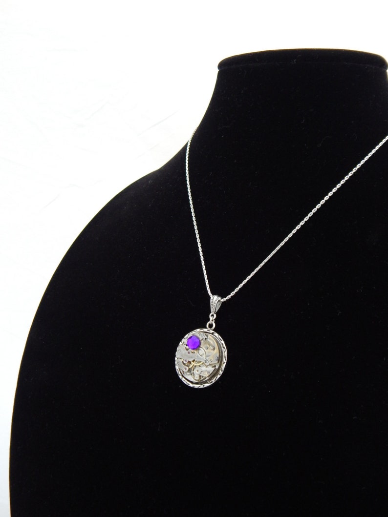May include: A silver necklace with a round pendant featuring a purple gemstone and intricate clockwork details.