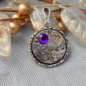 May include: A silver pendant with a purple gemstone set in a circular watch face with visible gears and the text "17 Jewels Swiss Made".
