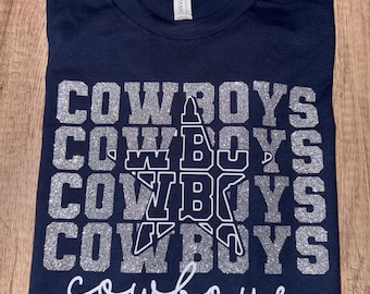 May include: A navy blue t-shirt with a silver glitter design that says "COWBOYS" multiple times. The word "cowboys" is also written in white cursive at the bottom of the shirt.