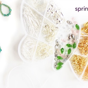 May include: Teardrop-shaped earrings with green beads and a dark gem, displayed with jewelry-making supplies in a butterfly-shaped organizer. The word "spring" is written in purple.