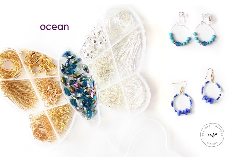 May include: A white butterfly-shaped organizer filled with jewelry-making supplies, including gold and silver wires, chains, and blue-green beads. Two pairs of earrings with blue accents are displayed. The word "ocean" is written in purple.