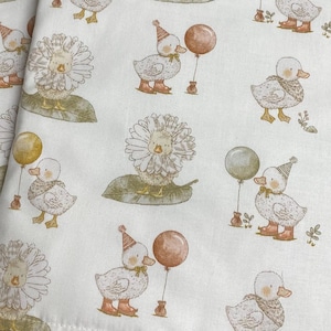 May include: Two rectangular fabric placemats featuring an off-white background with a repeating pattern of illustrated ducks. The ducks are depicted wearing party hats, standing on green leaves, or holding yellow and brown balloons.