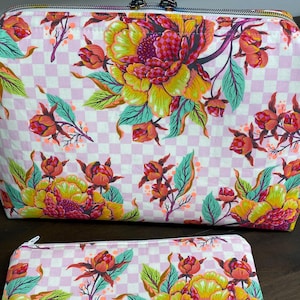 May include: A large structured pouch with a top zipper and a smaller flat rectangular pouch, both featuring a light pink and white checkered background pattern with vibrant yellow, orange, and red floral motifs and green leaves.