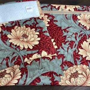 May include: A collection of fabric items featuring a floral pattern in burgundy, cream, and blue-green. The set includes a zipped pouch, a smaller pouch, and a rectangular item with a white patch. The floral design features large flowers and leaves.