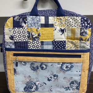 May include: A patchwork tote bag in navy, yellow, and white. The bag has a front pocket with a floral design and a zip closure. The handle is navy blue. The bag is handmade.