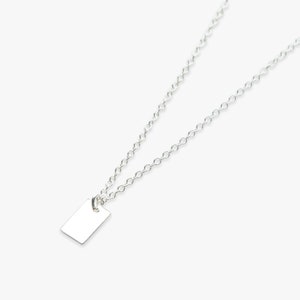 Puede incluir: Un collar de cadena de plata con un pequeño colgante rectangular.
