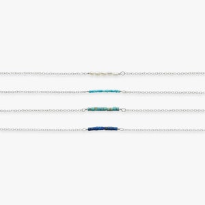 May include: Four delicate silver chains with different charms. The top chain has a row of white pearls, the second chain has a row of turquoise beads, the third chain has a row of turquoise beads, and the bottom chain has a row of blue beads.