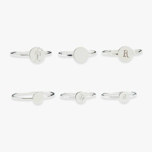 Op de afbeelding: Zes zilveren ringen met verschillende ontwerpen. De ringen hebben een palmboom, een lege cirkel, de letter R, een anker en de letter a.