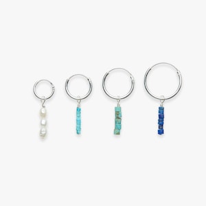 Könnte beinhalten: Set aus drei silbernen Creolen mit verschiedenen Anhängern. Der erste Ohrring hat einen Perlenanhänger, der zweite Ohrring hat einen Türkisanhänger und der dritte Ohrring hat einen Lapislazuli-Anhänger.