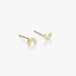 Op de afbeelding: Een paar gouden oorbel studs, elk met een eenvoudig halfrond ontwerp met een uitsparing in het midden.