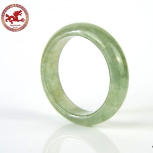 May include: A pale green jade ring with a smooth, polished finish. The ring is thick and has a rounded shape.