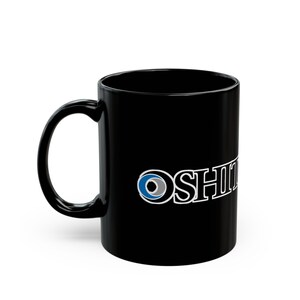 Puede incluir: Taza de cerámica negra con asa curva. La taza presenta la palabra "OSHII" en blanco, con un diseño circular azul y gris en el lado izquierdo del texto. La taza está diseñada para bebidas calientes.