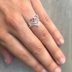 May include: A silver ring with a double heart design. The ring has a small red gemstone in the center.