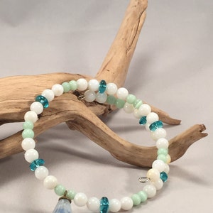 May include: A white and green beaded bracelet with a blue flower charm. The bracelet is made with white and green glass beads and a blue glass flower charm.