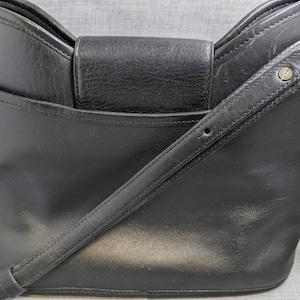 May include: Black leather crossbody bag with a flap closure and adjustable shoulder strap. The bag has a structured design with a front pocket and silver-tone hardware. A classic and versatile accessory for everyday use.