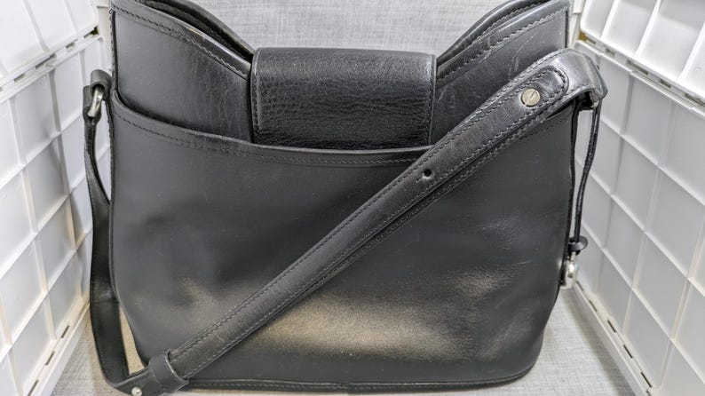 May include: Black leather crossbody bag with a flap closure and adjustable shoulder strap. The bag has a structured design with a front pocket and silver-tone hardware. A classic and versatile accessory for everyday use.
