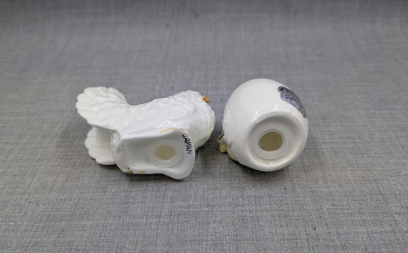 Puede incluir: Un juego de salero y pimentero de cer&aacute;mica blanca. Uno tiene forma de p&aacute;jaro con alas detalladas, el otro tiene forma de huevo. Ambos tienen agujeros para dispensar y est&aacute;n marcados "JAPAN".