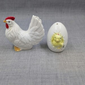 Puede incluir: Una figura de gallina de cer&aacute;mica blanca con cresta roja y pico amarillo se encuentra junto a una figura en forma de huevo blanco con un pollito amarillo que emerge. Son objetos decorativos.