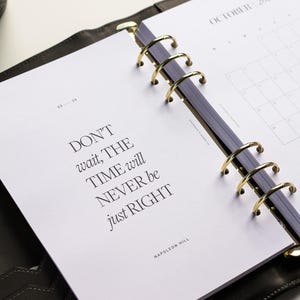 May include: Open planner with gold rings, featuring the quote "DON'T wait, THE TIME will NEVER be just RIGHT" by Napoleon Hill. The October 2026 calendar is visible. A gold pen rests nearby.