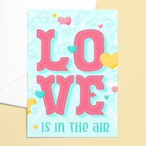 May include: A greeting card with the word "LOVE" in pink, surrounded by hearts and clouds on a light blue background. The phrase "IS IN THE AIR" is at the bottom. The card is paired with a white envelope.