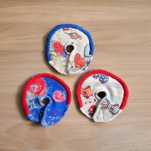 May include: Three fabric circles with red trim and a hole in the center. Each circle has a different colorful pattern.