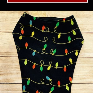 May include: A black bib with a pattern of colorful Christmas lights on a string. The bib has a rounded neckline and is made of a soft, comfortable fabric.