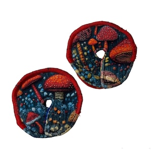 May include: Two round fabric patches with a red border and a dark blue background. The fabric features a repeating pattern of red and white mushrooms with green and yellow accents.