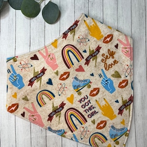May include: A beige bandana with a colorful pattern featuring rainbows, hearts, peace signs, roller skates, and the text "GRL PWR" and "You got this, girl".