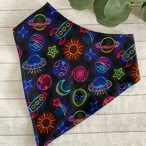 May include: A black bandana with a neon space-themed print. The print features planets, stars, rockets, and aliens.