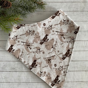 May include: A white bandana with a brown airplane pattern. The bandana features various airplane parts labeled with words like "cycle", "flight", "radar", "wingtip", "alpha", "takeoff", "harness", "sortie", "propeller", "rudder", "empennage", and "fighter".