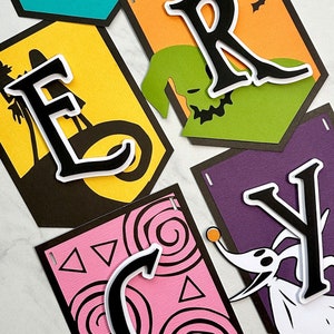 Puede incluir: Un banner de Halloween con la palabra "MERCY" escrita en letras negras con contornos blancos. Cada letra est&aacute; sobre un fondo de color diferente con un dise&ntilde;o de tem&aacute;tica de Halloween. Las letras est&aacute;n unidas entre s&iacute; con una cuerda negra.