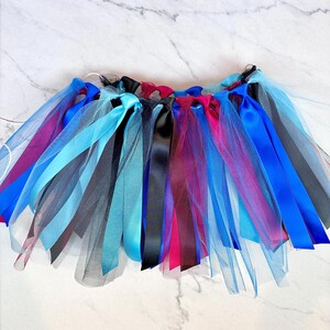 May include: A vibrant tutu skirt with layers of tulle and satin ribbons. The skirt features blue, black, pink, and purple ribbons. The tulle is light blue and black. Suitable for dance or costume purposes.