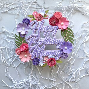 Op de afbeelding: Paarse en roze papieren bloemen caketopper met de tekst "Happy Birthday Mommy" in paarse schrijfletters.