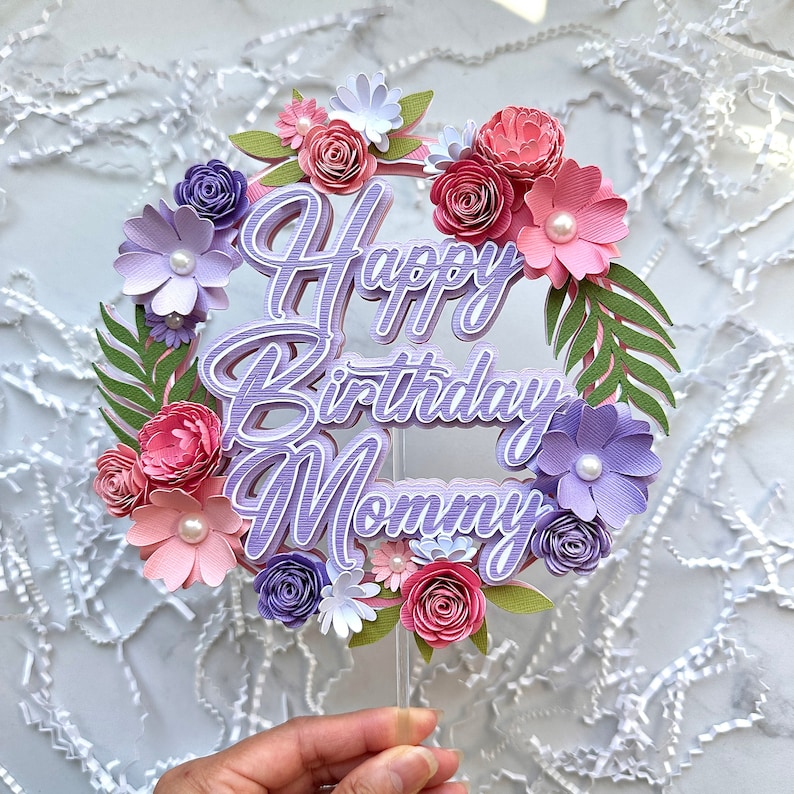 Op de afbeelding: Taarttopper van papier met paarse en roze bloemen en de tekst "Happy Birthday Mommy" in paars.
