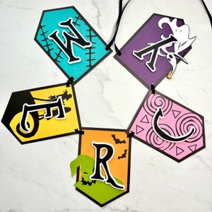 Puede incluir: Un bander&iacute;n de Halloween con la palabra "WRECKED" escrita en letras negras sobre banderines de papel de colores. Cada bander&iacute;n presenta un dise&ntilde;o diferente, incluyendo una silueta en blanco y negro de una bruja montando una escoba, un monstruo verde con una boca cosida, un bander&iacute;n morado con una silueta en blanco y negro de Jack Skellington y un bander&iacute;n rosa con un dise&ntilde;o de remolino negro.