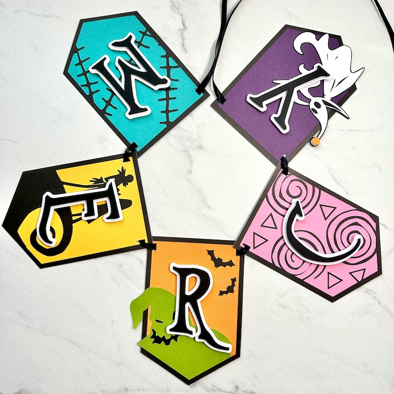 Puede incluir: Un bander&iacute;n de Halloween con la palabra "WRECKED" escrita en letras negras sobre banderines de papel de colores. Cada bander&iacute;n presenta un dise&ntilde;o diferente, incluyendo una silueta en blanco y negro de una bruja montando una escoba, un monstruo verde con una boca cosida, un bander&iacute;n morado con una silueta en blanco y negro de Jack Skellington y un bander&iacute;n rosa con un dise&ntilde;o de remolino negro.