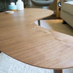 May include: A light brown, crescent-shaped coffee table with a smooth, wood grain surface.