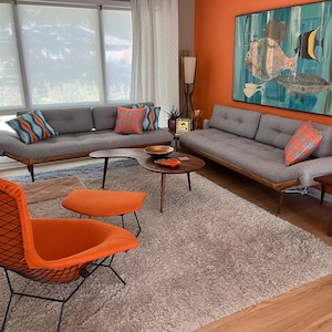 May include: A living room with a gray sofa, two orange chairs, a coffee table, and a side table. The walls are painted orange and there is a large painting of fish on the wall.