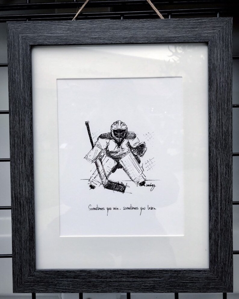May include: Black and white line drawing of a hockey goalie in a framed print. The print has the text "Sometimes you win. Sometimes you learn."