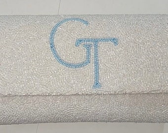 May include: A white beaded clutch with a blue embroidered "GT" monogram.