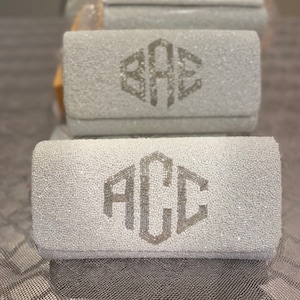 May include: Two white beaded clutches with silver monogrammed initials. The top clutch has the initials "BAE" and the bottom clutch has the initials "ACC".