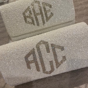 May include: Two white beaded clutches with silver monogrammed initials. The top clutch has the initials "SAE" and the bottom clutch has the initials "ACL".