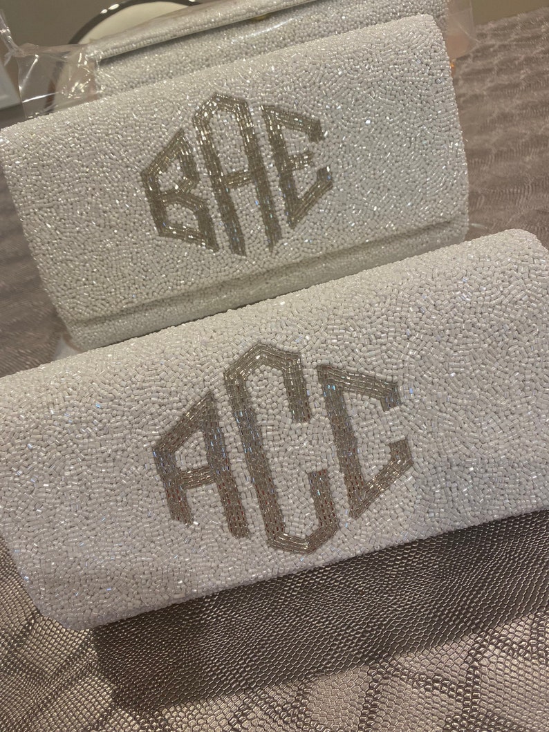 May include: Two white beaded clutches with silver monogrammed initials. The top clutch has the initials "SAE" and the bottom clutch has the initials "ACL".